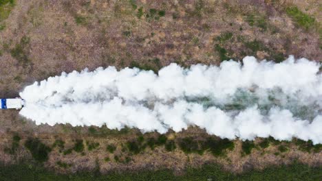 Truck-spreading-white-chemical-fertiliser-on-land,-top-down-aerial