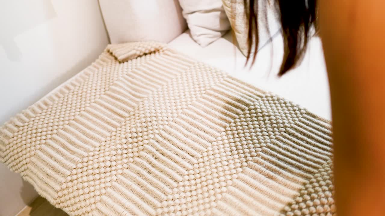 Una donna stende e sistema con cura un tappeto spesso, testurizzato, beige e tessuto su un divano.