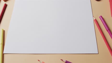 Overhead-view-of-blank-sheet-of-paper-with-school-stationery-on-beige-background,-in-slow-motion