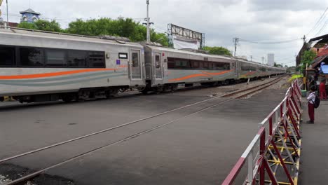 indonesia, yogyakarta, traffic is stopped while the train is passing,first locomotive than train carriages passes, a student waiting for the train to pass to get across the street.traffic moves slowly