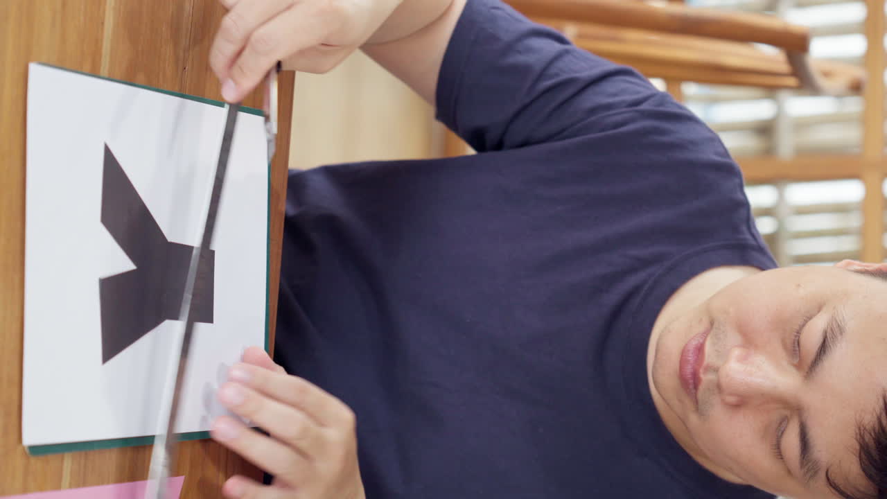 아시아인 남자가 카팅 매트에 러를 가진 유리티 칼 커터를 사용하여 종이를 잘라서 diy 공예 프로젝트를 하고 있습니다.