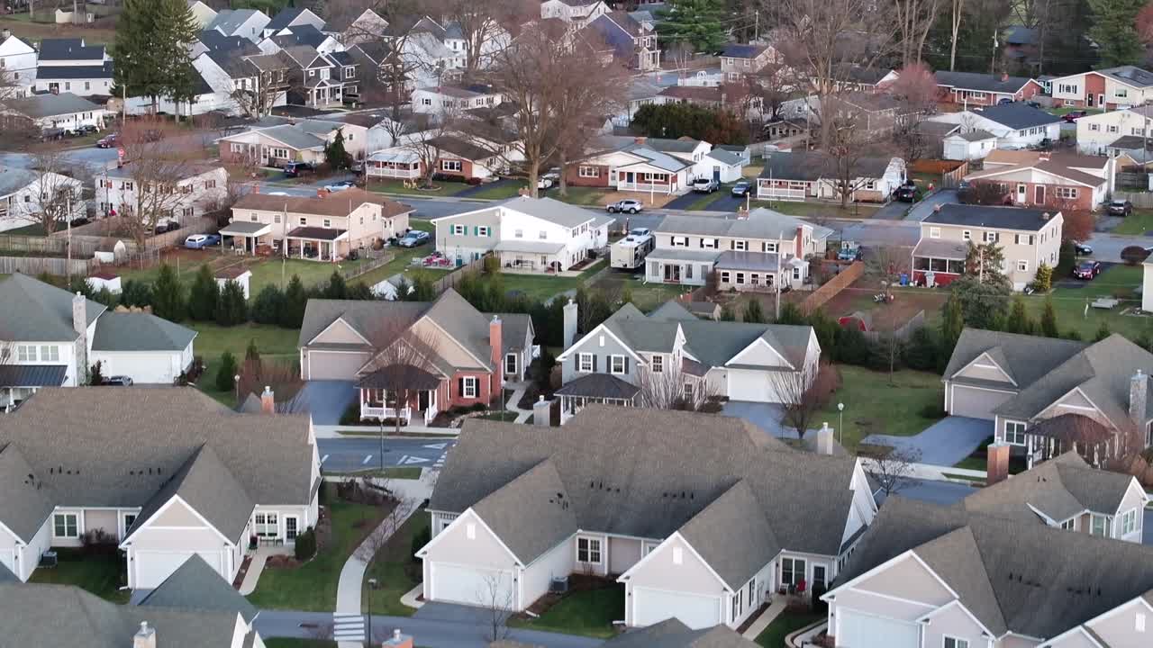 American residential area with new build homes in suburb of USA. Aerial rising wide shot. Cold winter day. Premium settlement with luxury villas at sunset. Leafless trees at dusk.