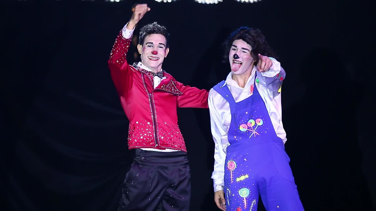 Pair of clowns high fiving and bowing and thanking the public in a dark background during a circus performance