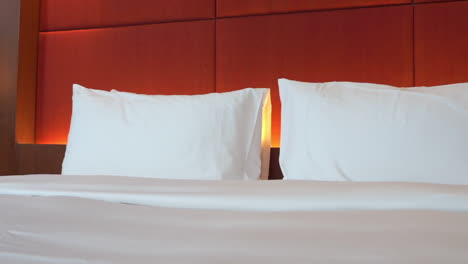 modern bedroom, led light behind white pillows and kingsize bed in upscale hotel pan left