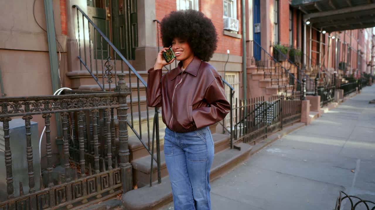 Woman in stylish urban outfit talking on phone on city street