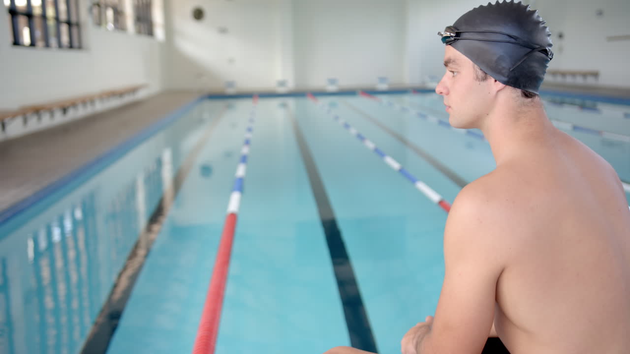 male swimmer in swim cap sitting by pool, preparing for practice session, copy space
