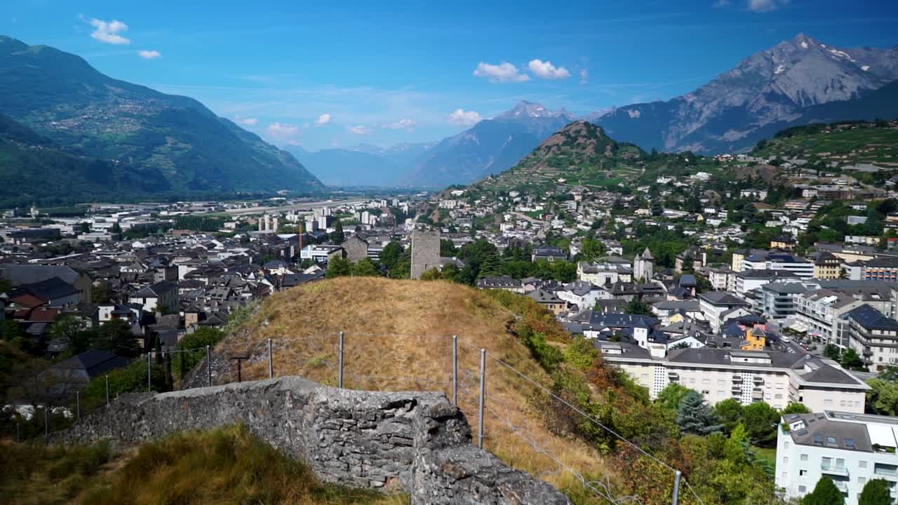 Reveal shot of Swiss Alps city in valley between beautiful mountain ranges with stone wall