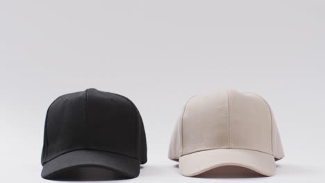 Video-of-black-and-beige-baseball-caps-and-copy-space-on-white-background