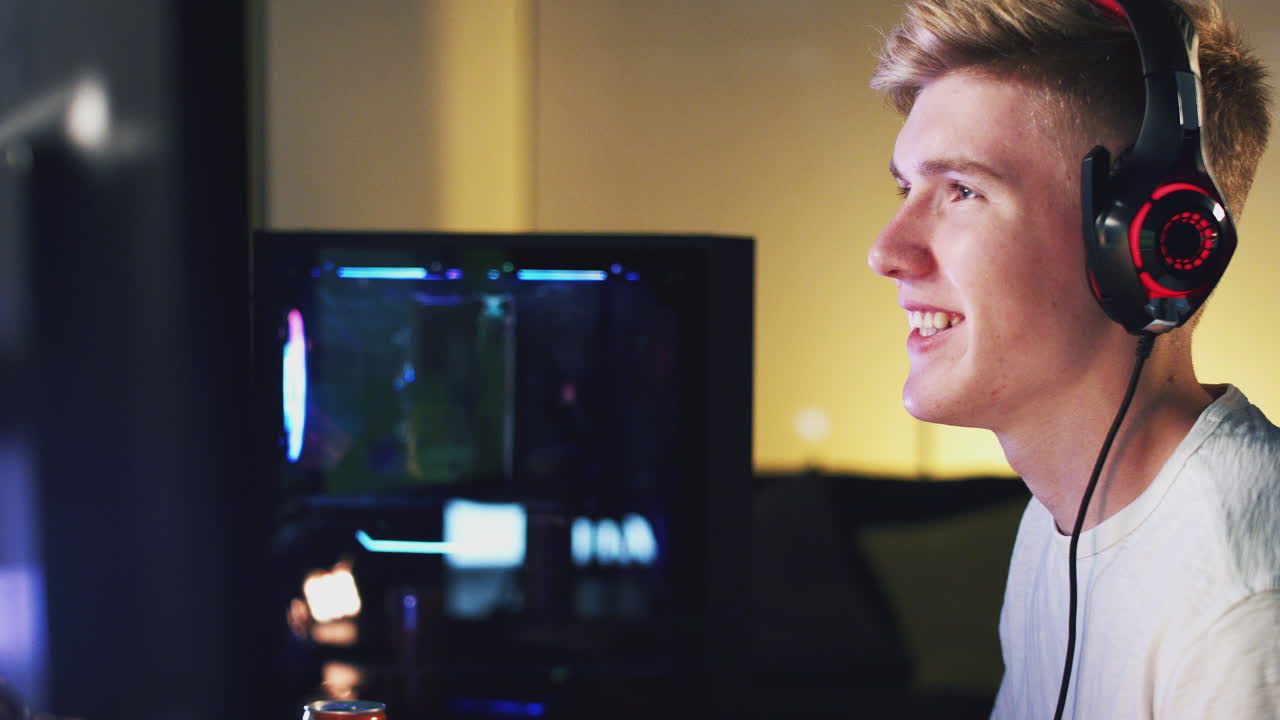 Teenage Boy Wearing Headset Gaming At Home Using Dual Computer Screens