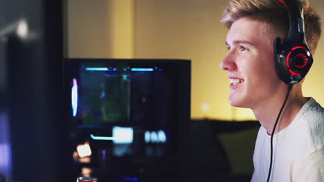 teenage boy wearing headset gaming at home using dual computer screens