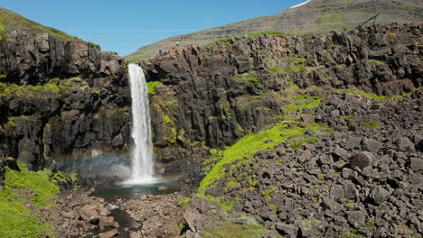 Icelandic-waterfall-with-icy-cold-water-on-a-sunny-day,-aerial-view