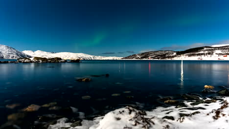 green northern lights flare over water and snowy terrain, skogsfjord. time lapse