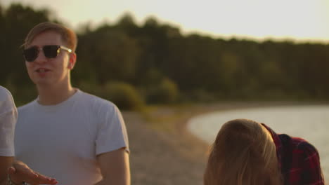 Company-of-young-students-celebrate-the-end-of-the-semester-with-beer.-This-is-carefree-summertime.-They-dance-and-sing-songs-on-the-open-air-party-on-the-sand-beach.