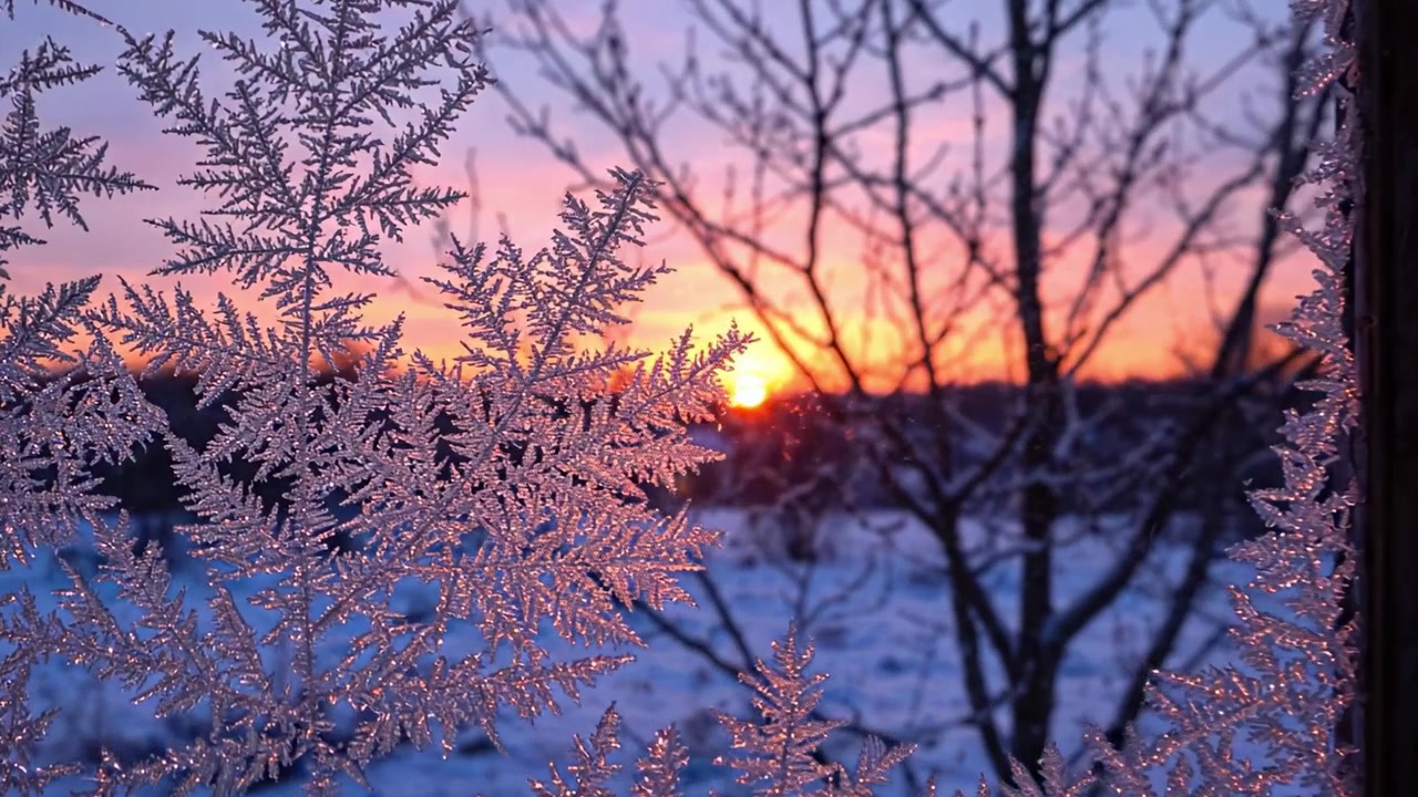 En vintersolopgang gennem frostklart glas: Fascinerende snefnugmønstre indrammer en farverig daggry over et fredfyldt snelandskab.