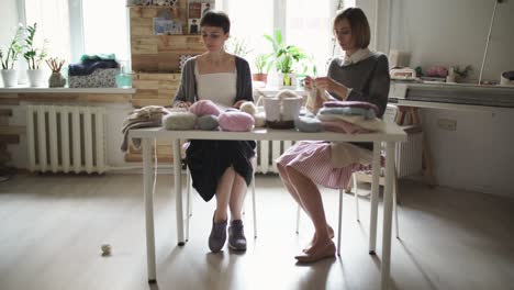 Two-knitting-woman-making-wool-fabric-sitting-at-table-in-textile-workshop