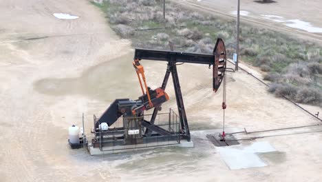 Un-Bombeo-De-Petróleo-En-Movimiento-En-Un-Campo-Desolado,-Día-Nublado,-Paisaje-Industrial,-Vista-Aérea