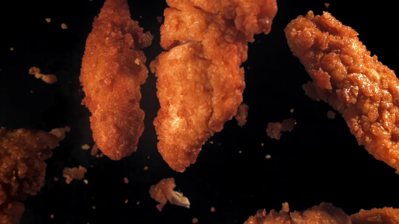 Potongan Ayam Goreng Renyah Jatuh dengan Latar Belakang Gelap