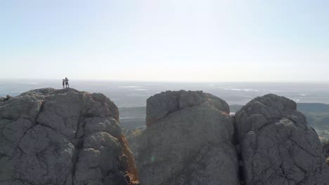 Drone-shot-of-mountainous-terrain,-hikers-and-cityscape-in-the-distance