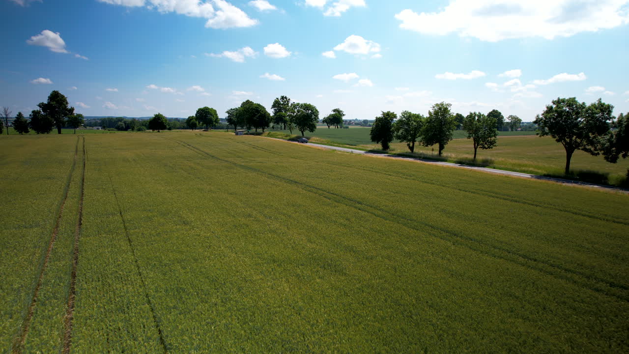 el coche pasa rápido por una carretera de campo pintoresca junto a la tierra de la granja, el cielo azul, el dolly aéreo