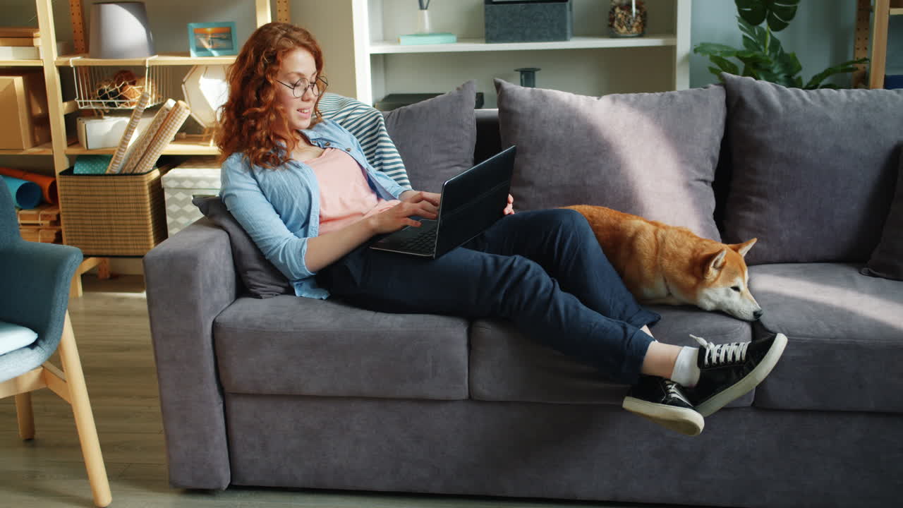 Woman working on laptop with dog on couch
