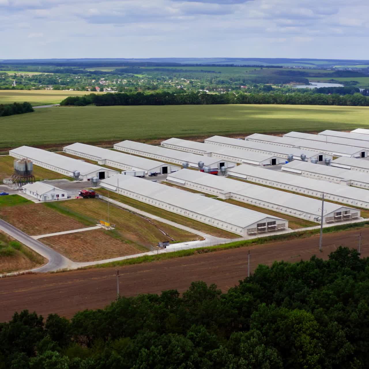 Farm among beautiful green nature. Modern white farm buildings in environment in summer. Agricultural complex on field