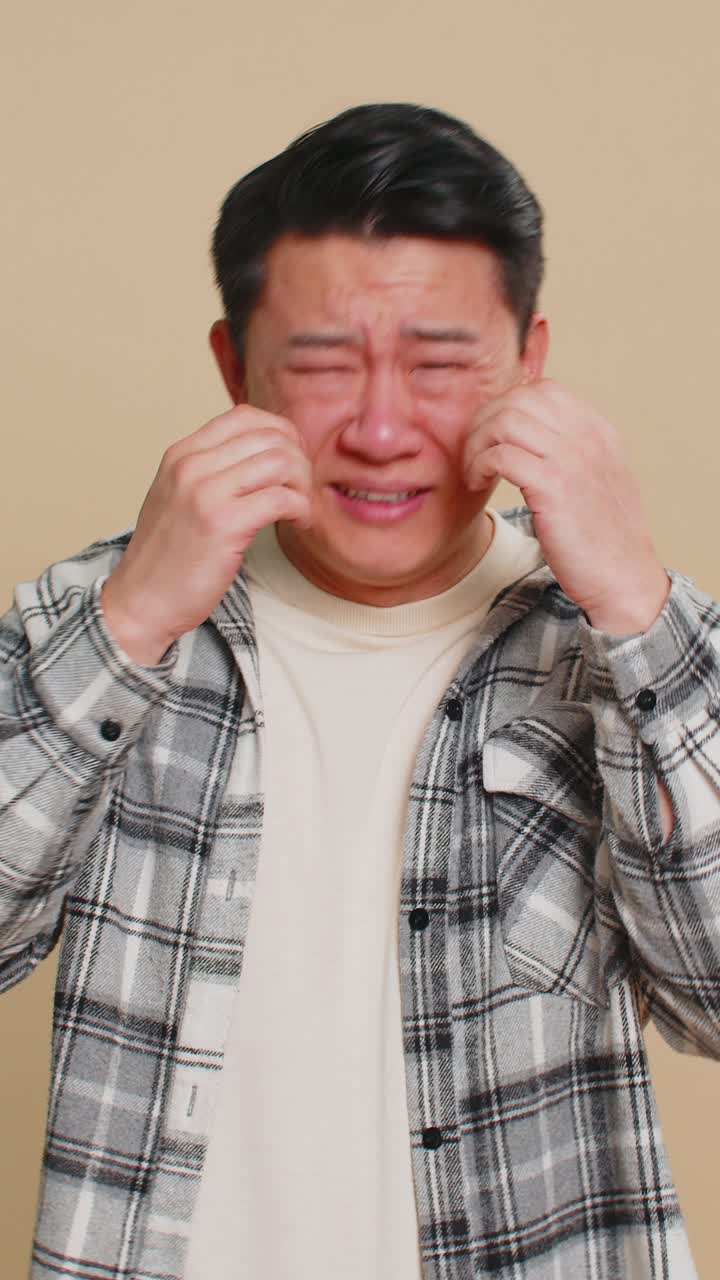 Upset disappointed asian man wipes tears and cries from despair being sad because of unfair things