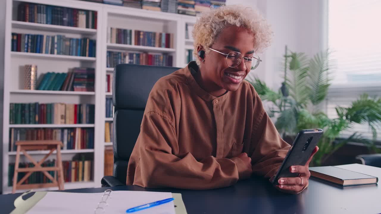 Joyful young african woman make answer video call on phone at home office