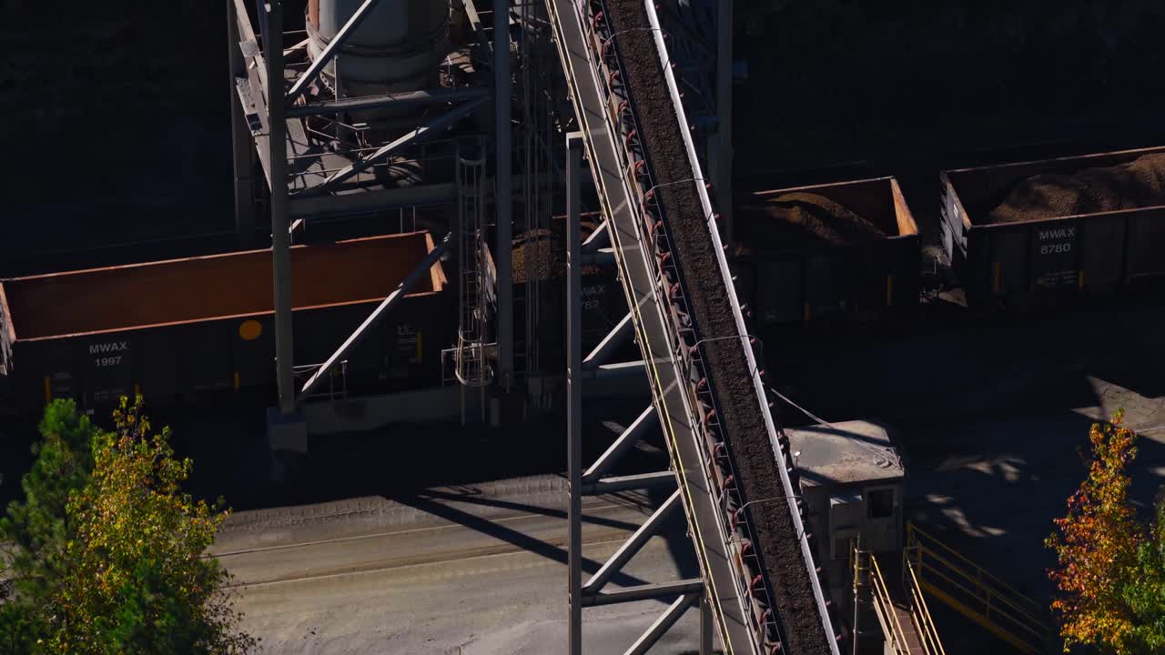 Aerial ascend of rail line running alongside quarry site transporting gravel to train via conveyor belt