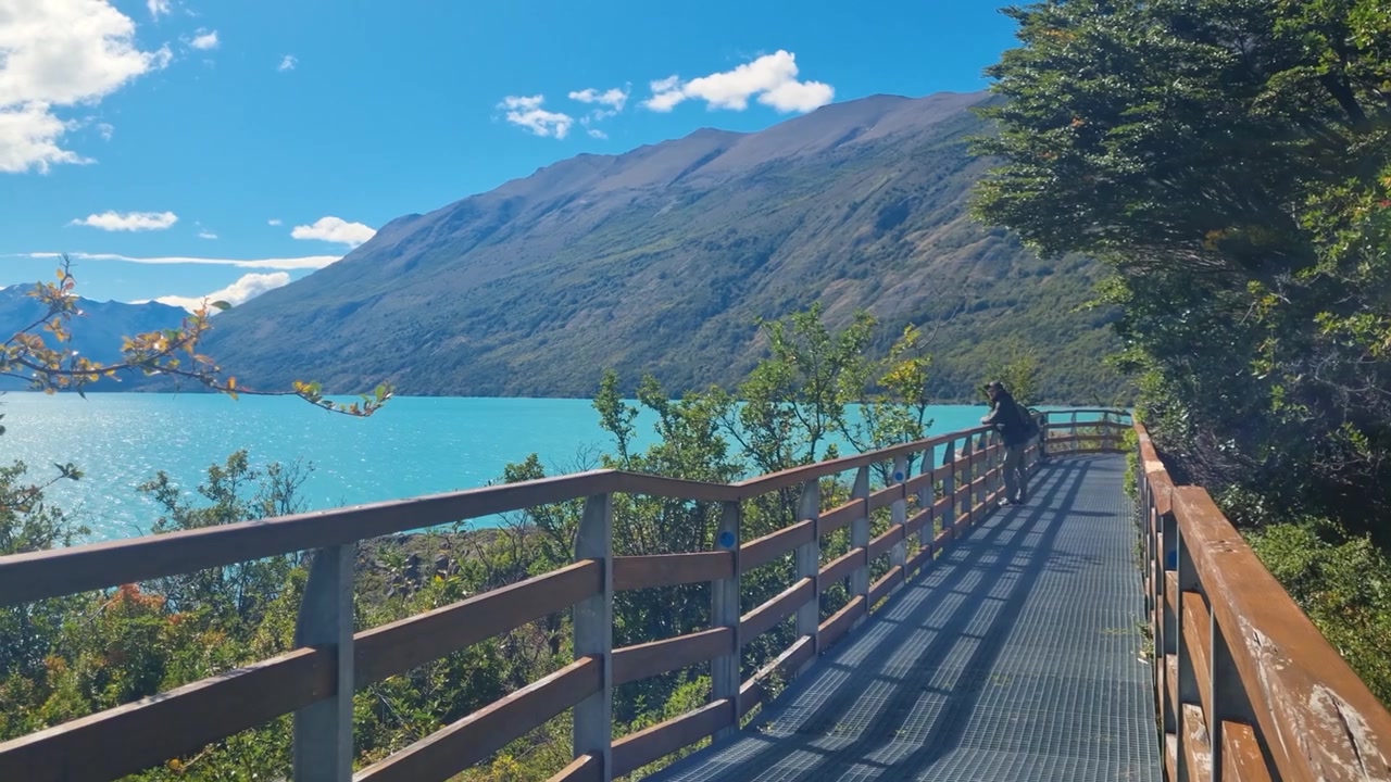 Un escursionista cammina lungo la passerella di legno accanto al Lago Argentino, fermandosi ad ammirare il mozzafiato paesaggio patagonico dopo aver visitato il Ghiacciaio Perito Moreno in una giornata limpida