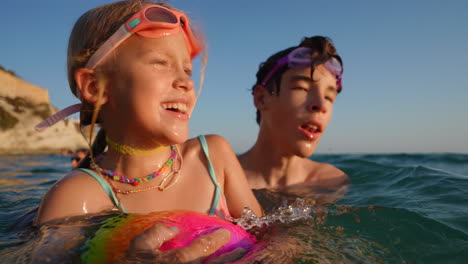 brother and sister splashing playfully in sparkling ocean waters, wearing vibrant swimming goggles and colorful necklaces during summer vacation moments of pure childhood joy