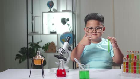 cute little scientist looking at liquid in test tube and showing thumb up