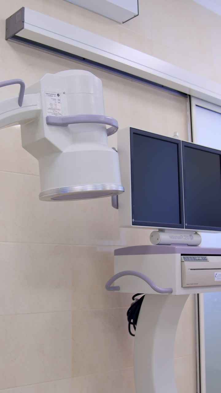 C-Arm fluoroscopy machine standing in the modern surgery room. Operational table with lung ventilation system standing nearby. Vertical video