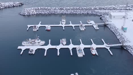 iceland harbor with boats docked at jetty covered in white snow, aerial