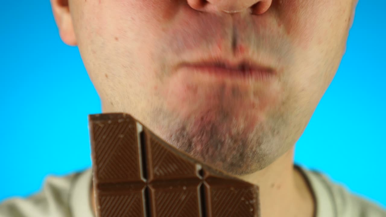 hombre mordiendo y comiendo una barra de chocolate. primer plano de la mitad inferior de la cara masculina, comiendo comida dulce