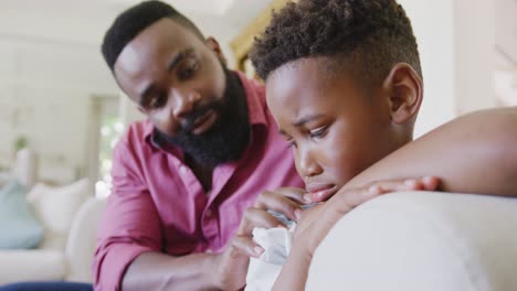 sad african american father and son sitting on sofa and embracing, in slow motion