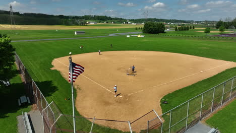 american flag waves in front of teens playing baseball