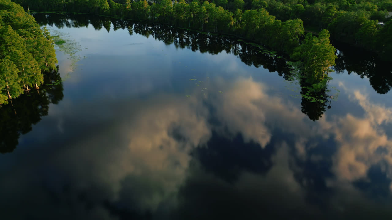 Drone dolly shot of the Hillsborough River with surrounding forest at dusk and sunset clouds reflected in water