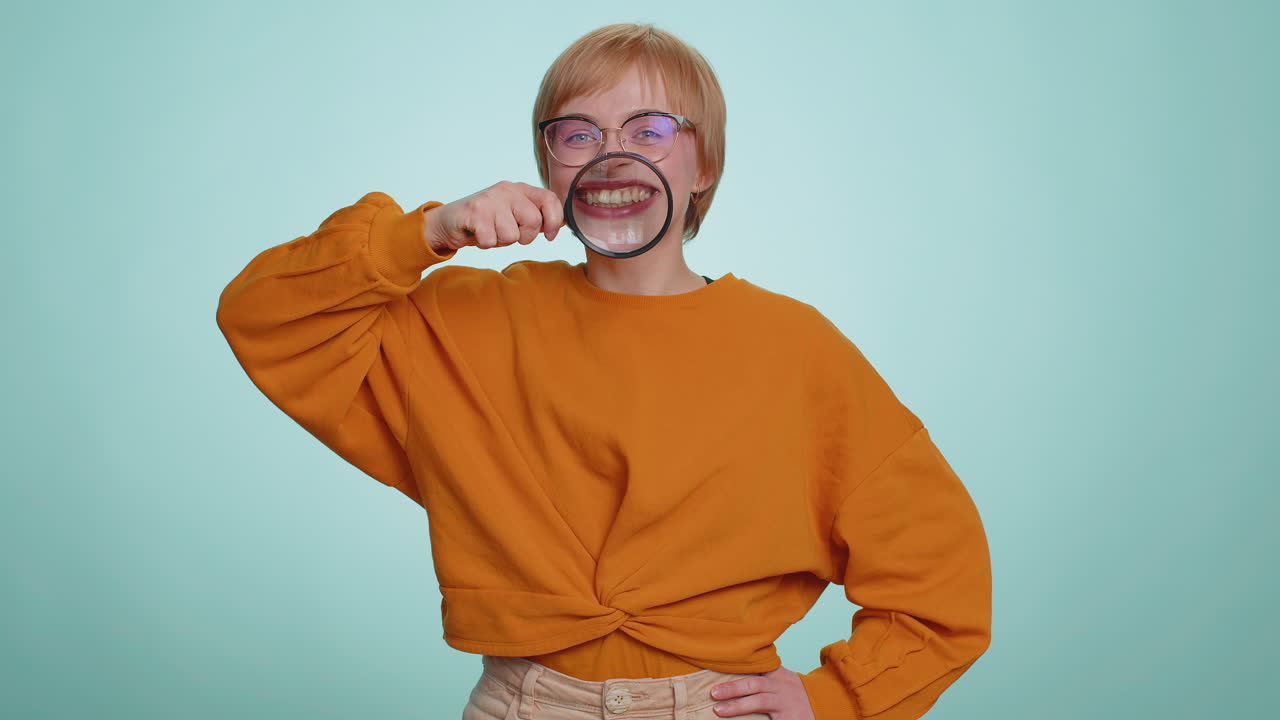Woman holding magnifier glass loupe on teeth looking at camera showing funny smiling face mouth