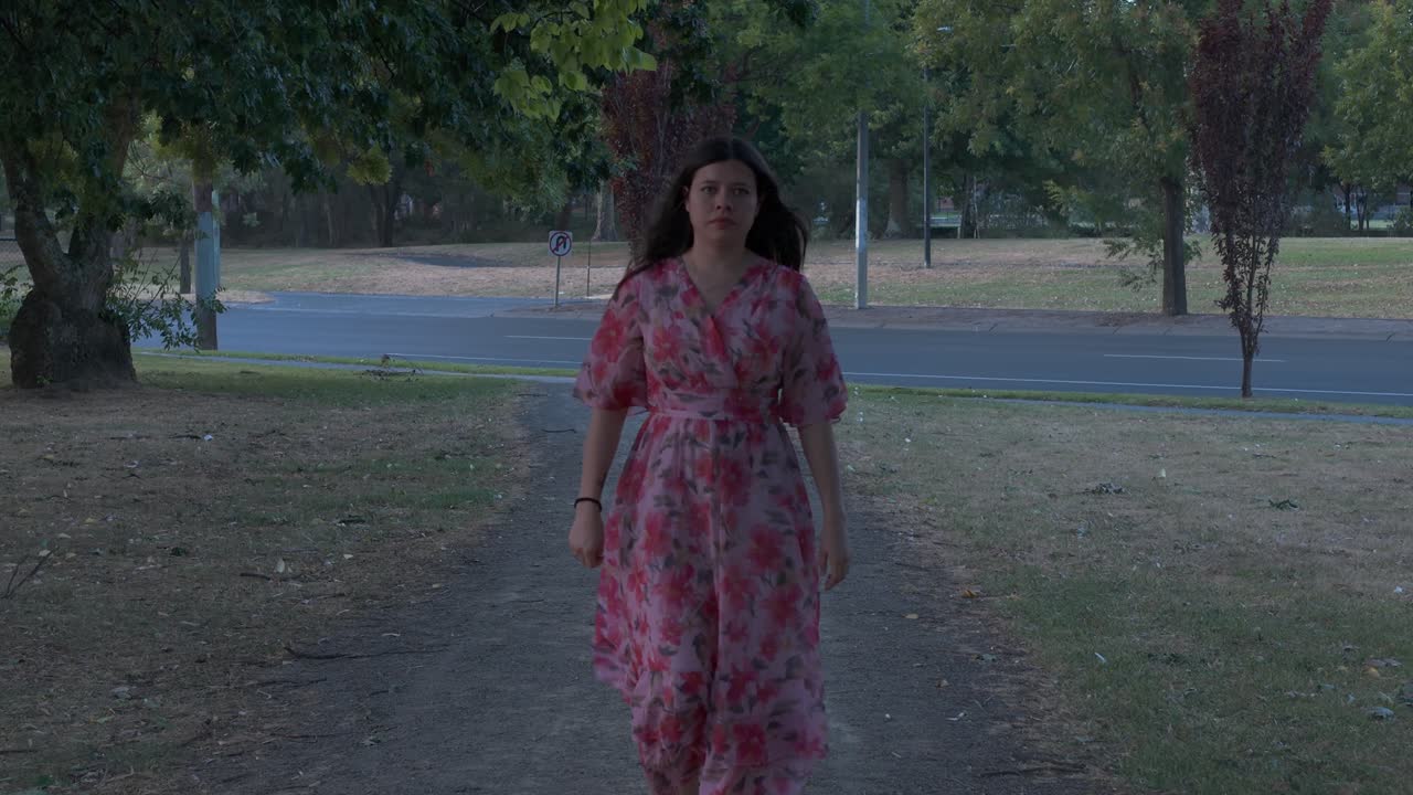 Una donna ispanica con un abito floreale rosa cammina con grazia attraverso Croydon Park a Melbourne. L'ambiente sereno è catturato con una morbida luce crepuscolare e una composizione pacifica.