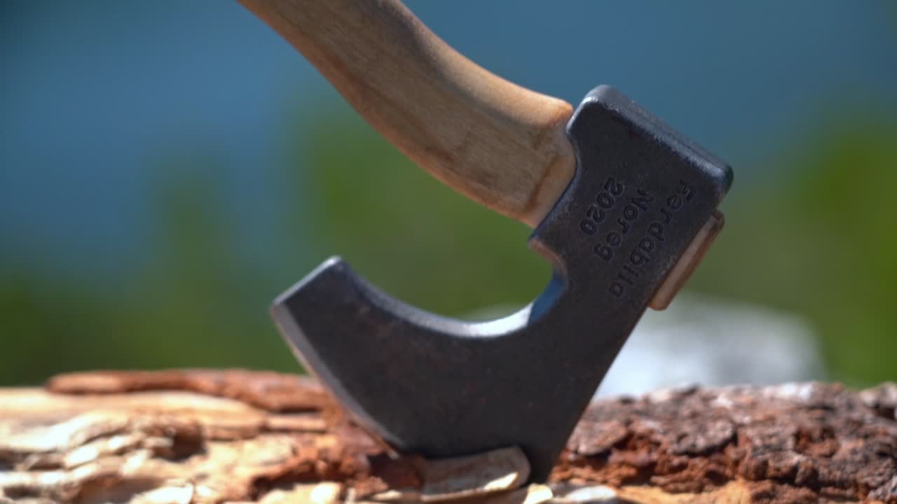 Closeup of hatchet inserted to firewood log - camera slowly moving upwards from steel blade to shaft with blurred shallow depth background - Sunny day handheld