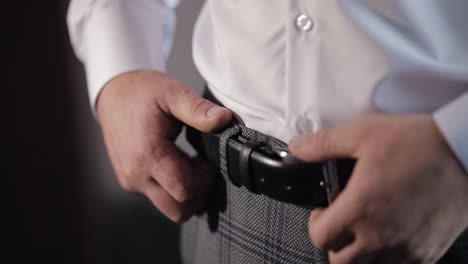 groom wears a belt. man in white shirt puts belt on pants in wedding morning. businessman prepare