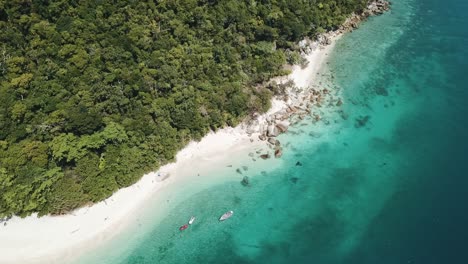 Drone-aerial-pan-up-with-boats-in-tropical-blue-clear-water-and-rocks-on-a-sunny-day