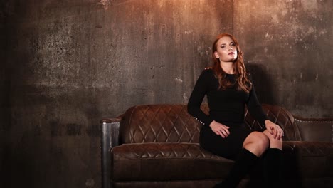 mujer de vestido negro sentada en un sofá de cuero