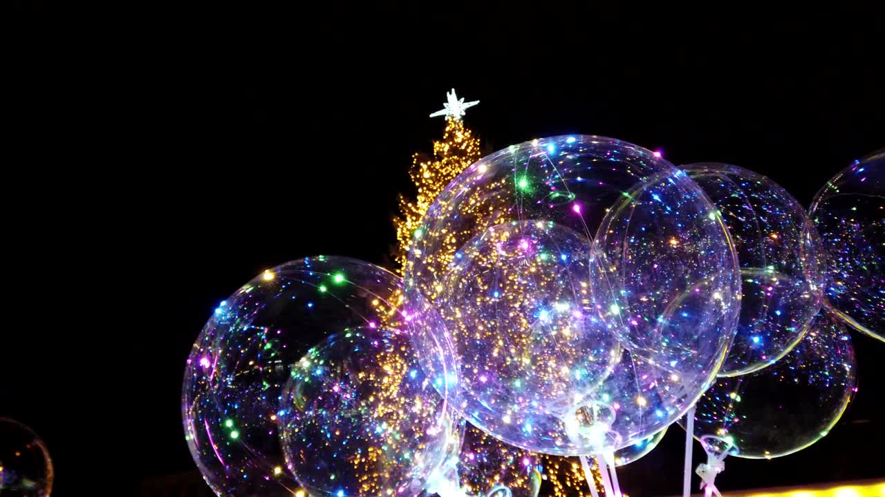 Balloner med guirlander mod juletræets baggrund. Gennemsigtig LED-ballon med flerfarvet lysende guirlande. Klare lys om natten.