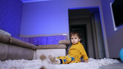 dark-haired baby boy sitting on the carpet. kid lies down in the plaid and rolls around.