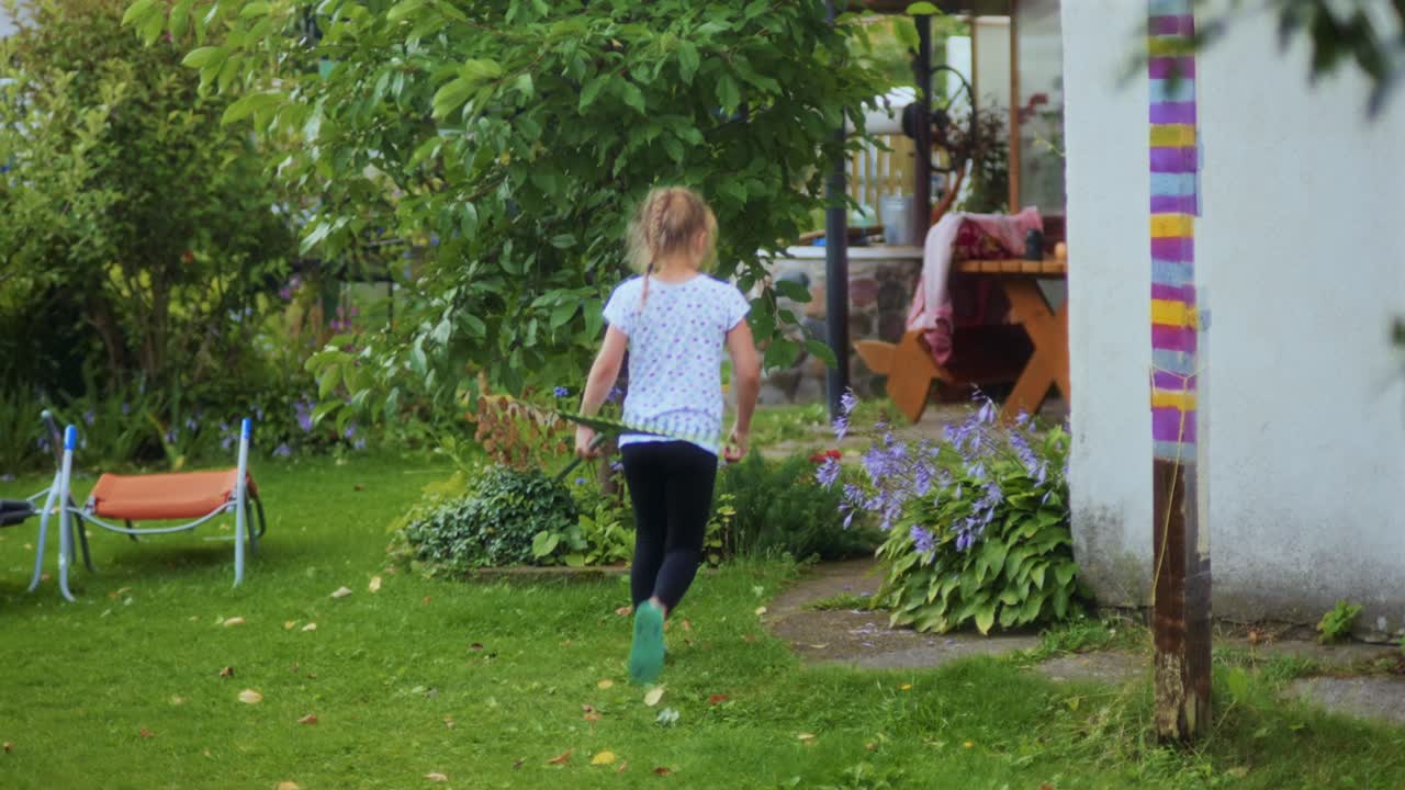 Young girl carrying a garden rake in the daytime in the garden ...
