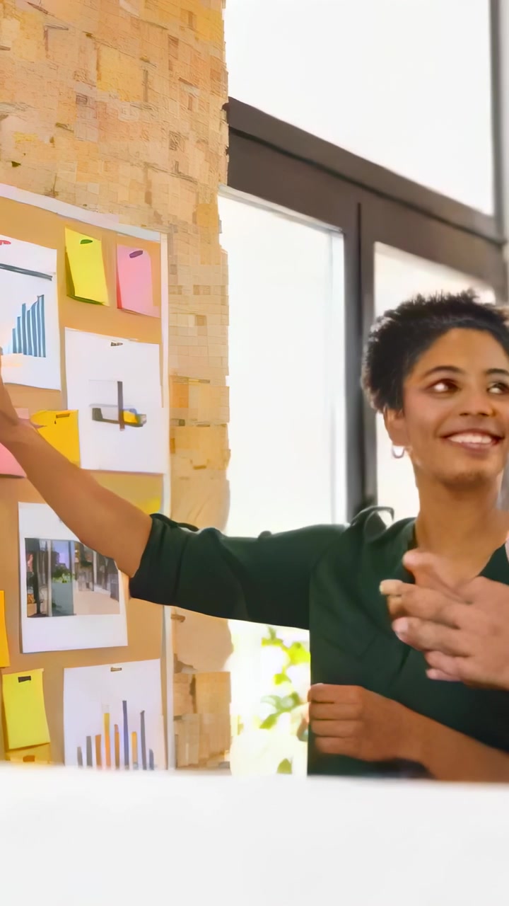 Vertical video: Planning, arranging woman green blouse adjusting sticky notes, charts at corkboard