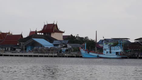 vista en 4k de un templo y un bote de madera anclados a lo largo del río de bang tabun, tailandia