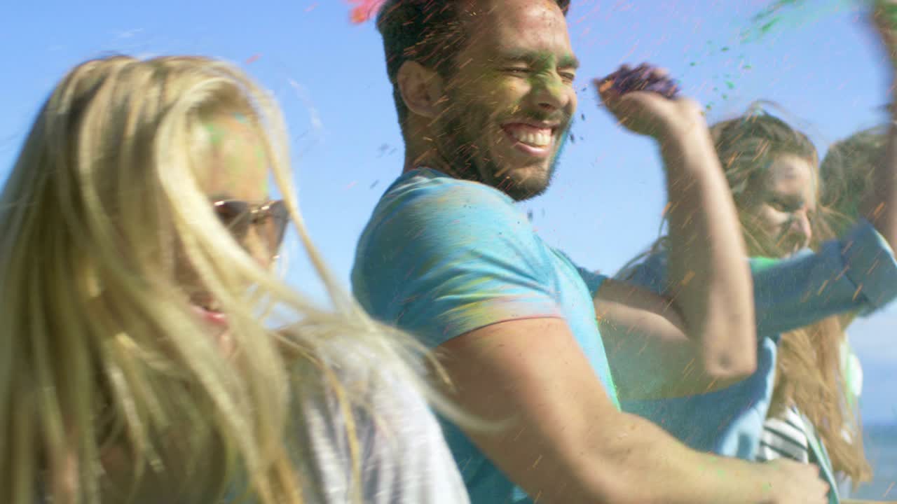 un grupo multiétnico de jóvenes se arrojan polvo de colores el uno al otro en celebración del festival de holi. se divierten enormemente en este día despejado junto al mar.