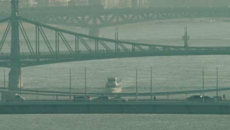 famous bridges in budapest with a boat driving on the danube